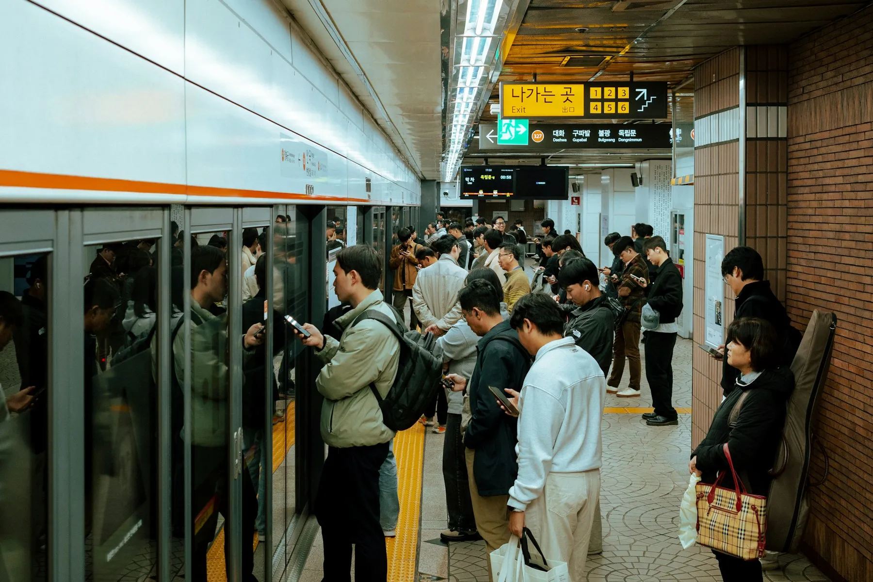 People waiting on a subway platform, most of them looking at phones